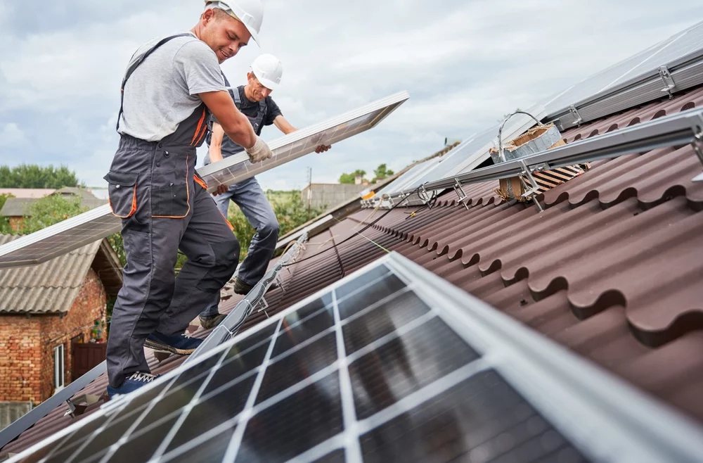 An MCS accredited professional carrying a solar panel towards a house on a bright, sunny day.