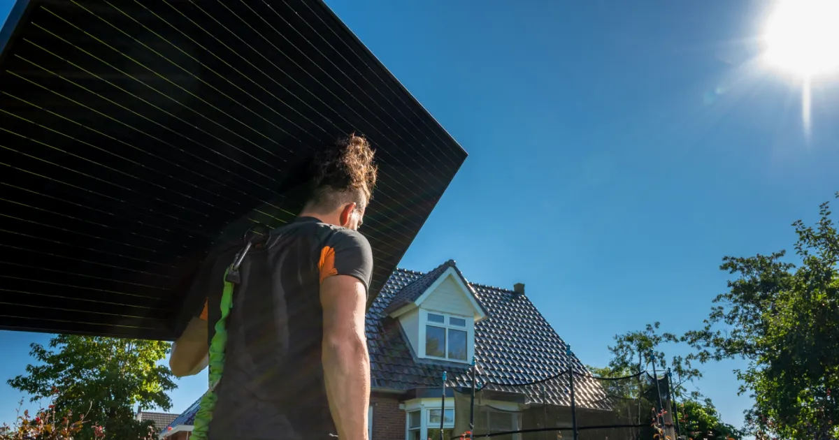 A Soly installer is carrying a solar panel in sunny weather.